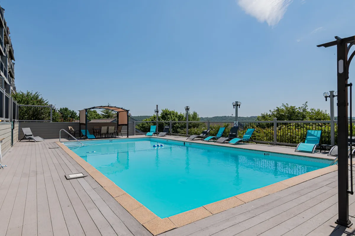 An inviting outdoor pool area with lounge chairs and a canopy-covered seating space, surrounded by greenery. The scene is set for family-friendly relaxation and fun under the sun.
