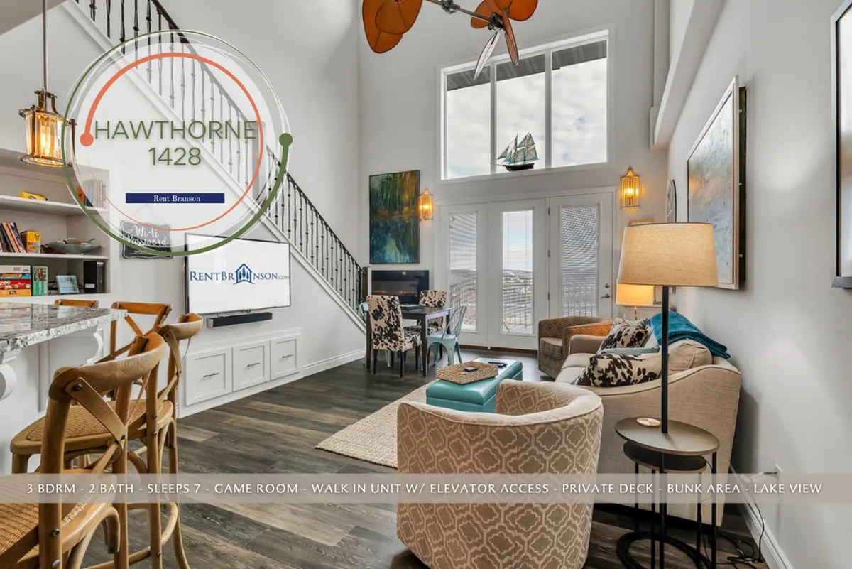 A bright and spacious living area with large windows offering spectacular views of the lake below, plush seating arranged for conversation or relaxation, and elegant lighting fixtures. An eye-catching staircase adds architectural interest, while the windows fill the room with natural light and emphasize the dramatic ceiling height.