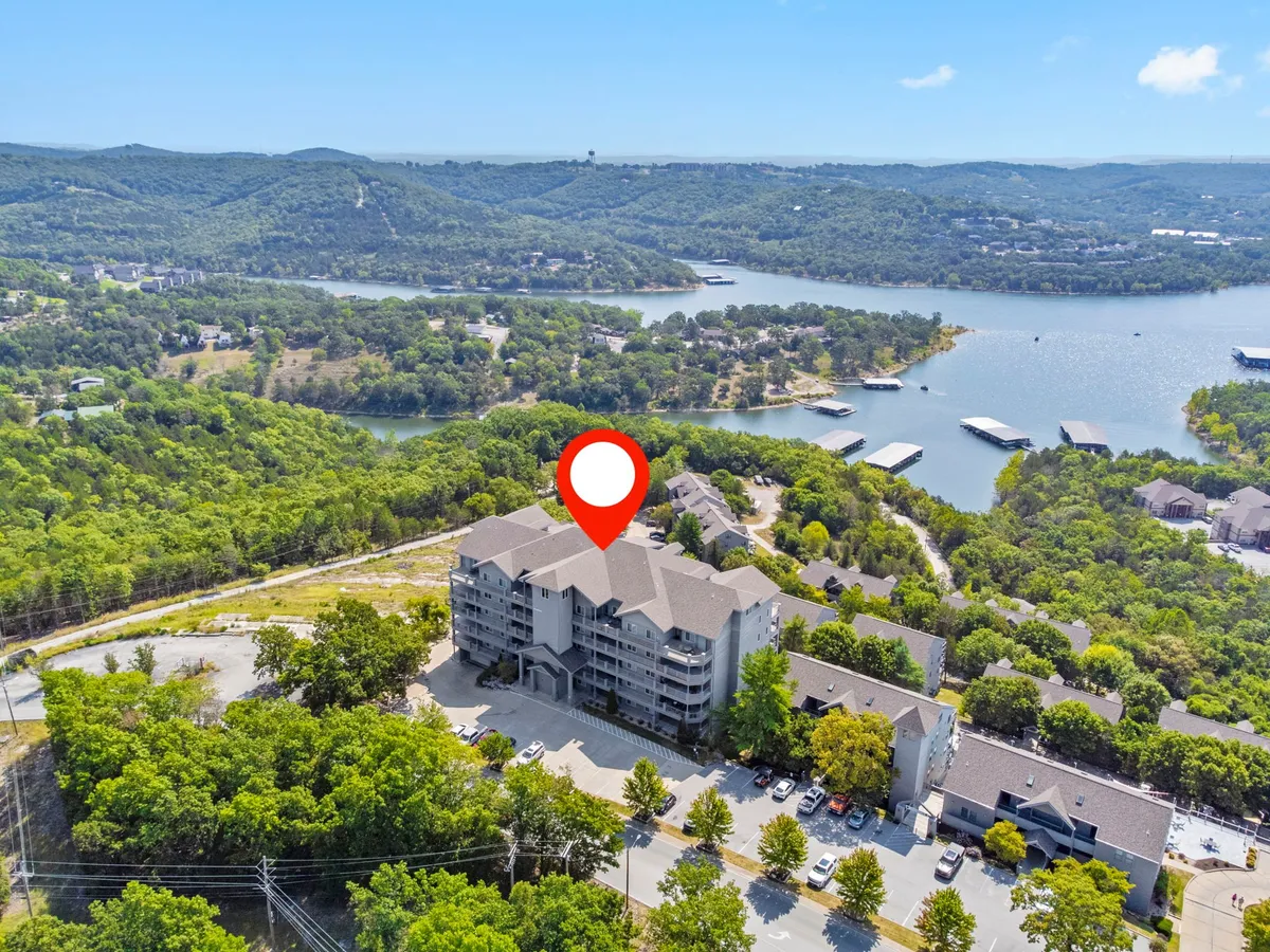 A wide-angle view of the condo building set against lush greenery, with Table Rock Lake and distant mountains in the background. The image emphasizes the natural beauty of the location and the inviting atmosphere of the property, with balconies visible for lake viewing.