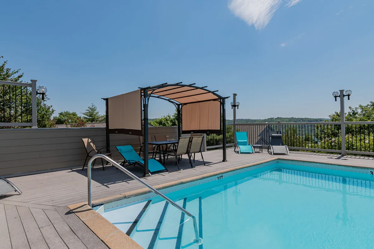 This image highlights the resort’s outdoor swimming pool framed by a canopy and lounge chairs, with inviting blue water and plenty of space for sunbathing or enjoying a swim. The pool area is surrounded by a landscaped setting that suggests both relaxation and summertime fun.