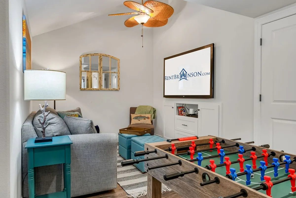 A playful and relaxed interior with a foosball table, sofa, table lamp, wall-mounted TV, and mirrored wall décor. The setting is ideal for both energetic games and unwinding with a movie or TV show.
