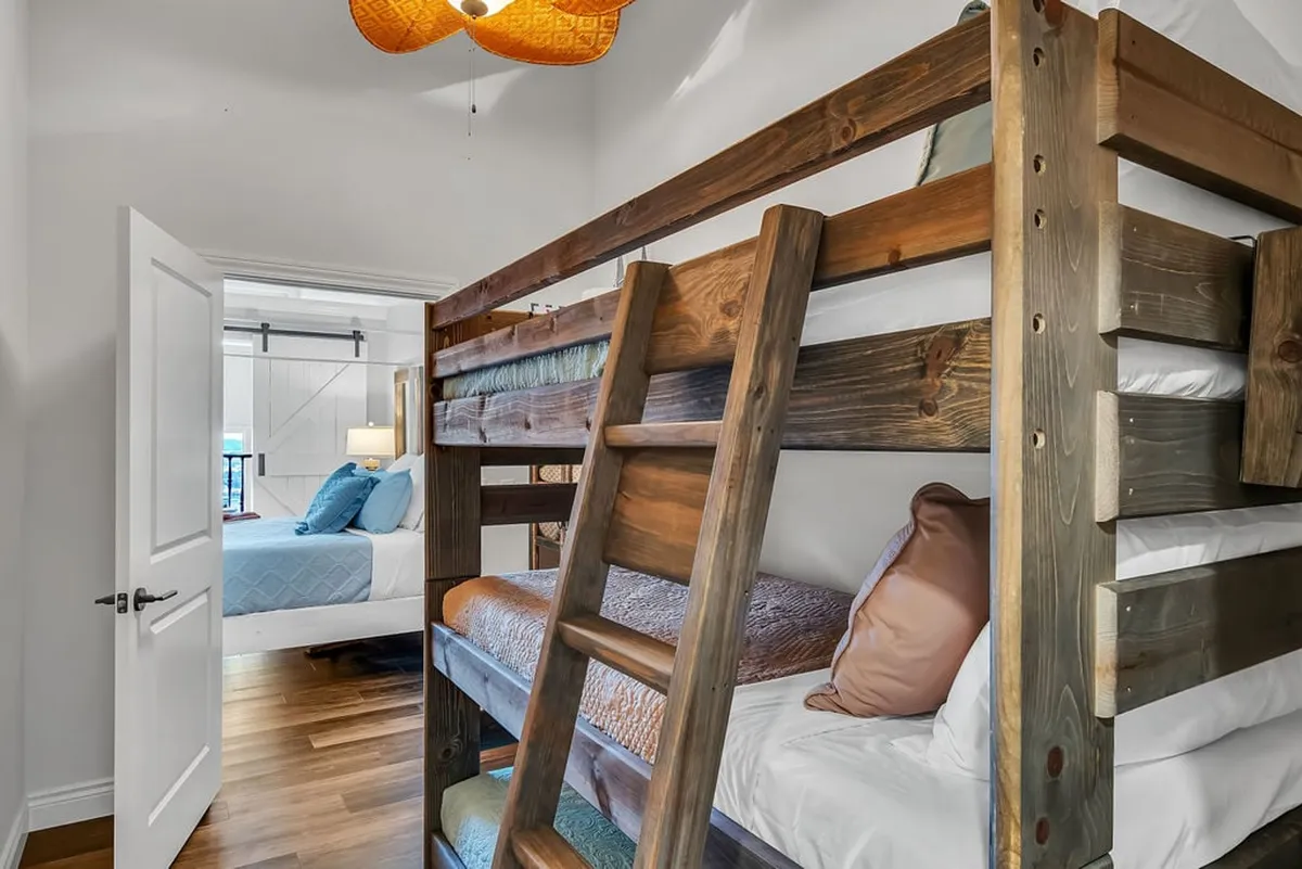 A playful bunk room featuring a sturdy bunk bed, a decorative light fixture, and a doorway leading to another room. The space is designed for fun sleepovers and family-friendly flexibility.