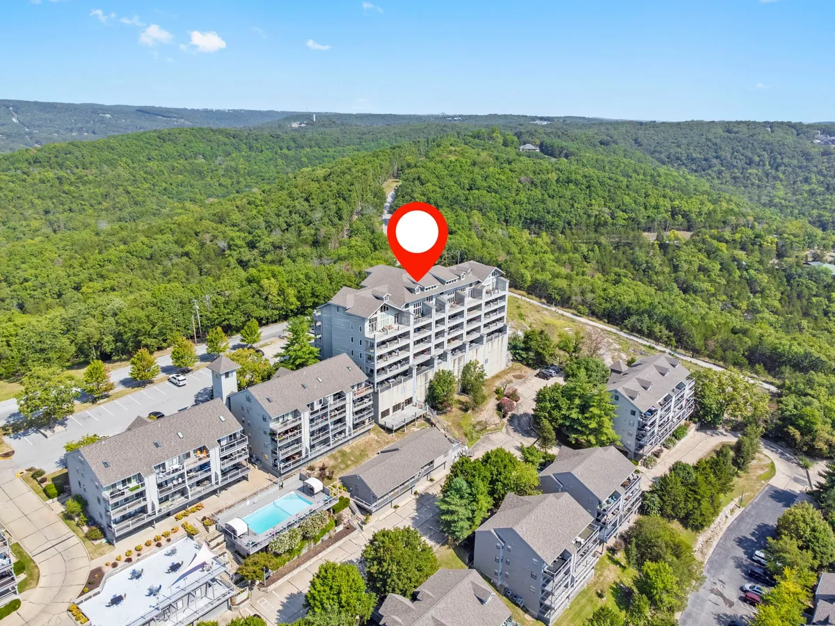The exterior of a multi-story condominium building is surrounded by lush greenery and features a refreshing swimming pool in the foreground, inviting guests to relax or socialize outdoors.