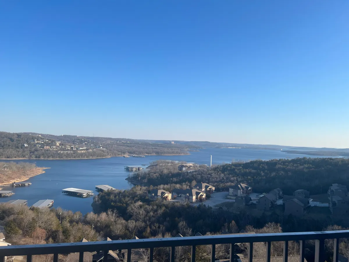 A breathtaking view from above, capturing the expanse of Table Rock Lake and the surrounding hills, with houses dotting the shoreline. The tranquil scene draws the viewer's eye to the panoramic beauty available from the living and deck areas.