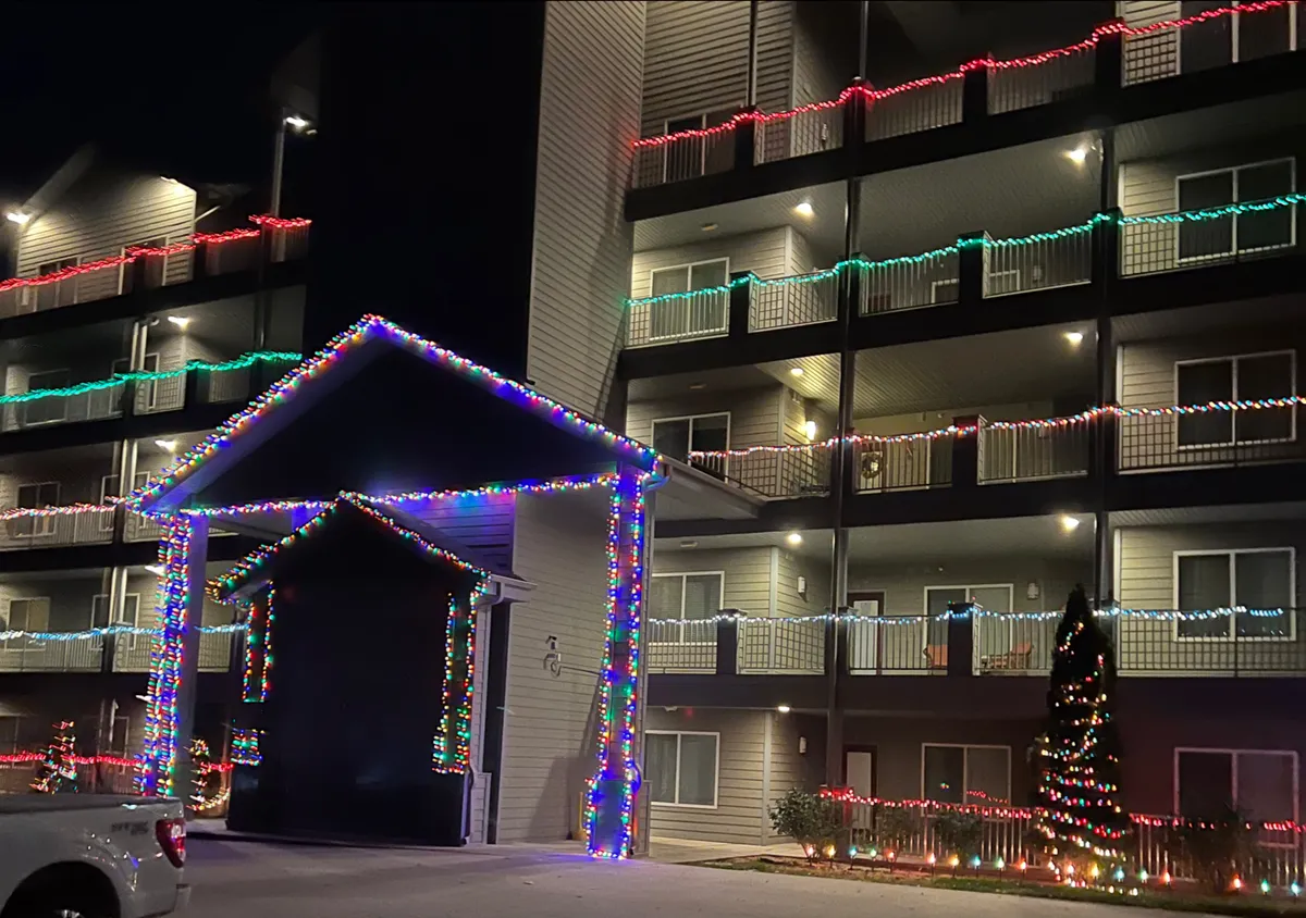 This image shows festively decorated building exteriors with Christmas lights, an entrance awning, a balcony adorned for the holidays, and a Christmas tree, creating a warm, celebratory atmosphere ideal for winter visitors.